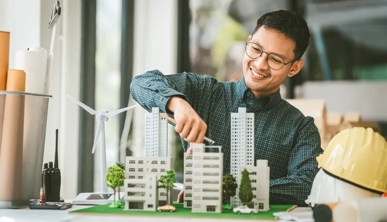 Digitale Zwillinge: Vernetzt, vorausschauend – und nachhaltig? // Asian man working with a 3D model of sustainable city with wind turbines