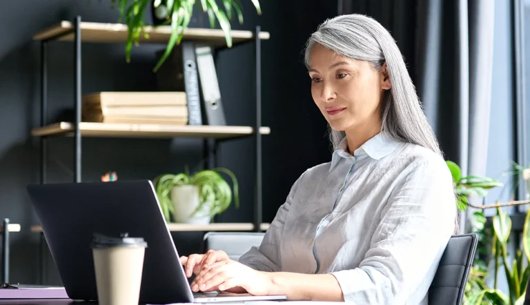 Wenn Erfahrung das Unternehmen verlässt: Wie KI das Wissen der Belegschaft sichert // Senior female, Asian businesswoman typing laptop computer in office