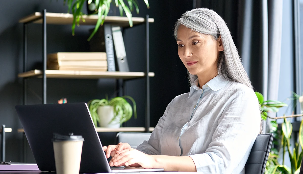 Wenn Erfahrung das Unternehmen verlässt: Wie KI das Wissen der Belegschaft sichert // Senior female, Asian businesswoman typing laptop computer in office